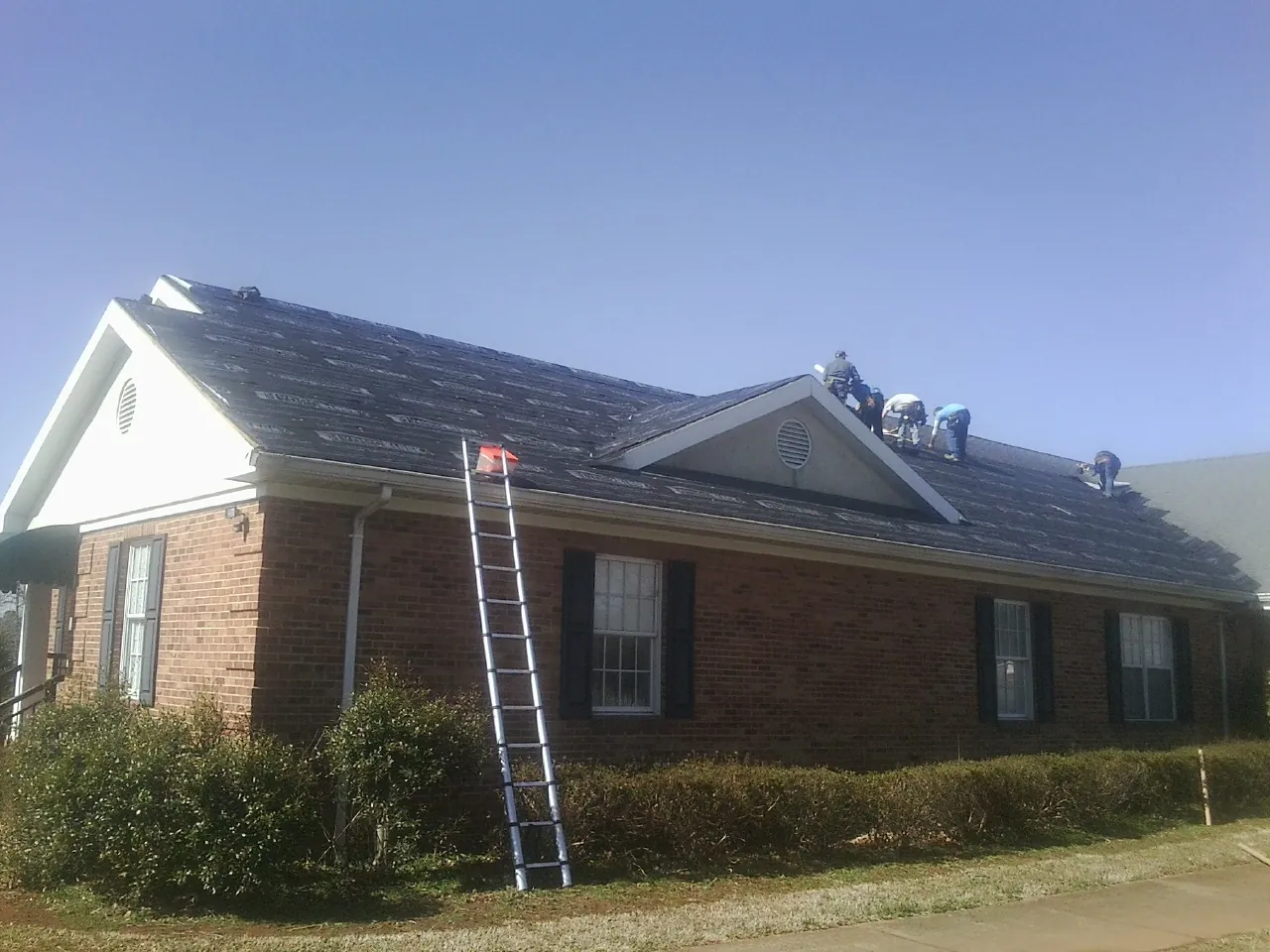 Crew tearing shingles off a brick ranch roof with a ladder set — Emergency Roof Repair work by our crew in Strawberry Plains