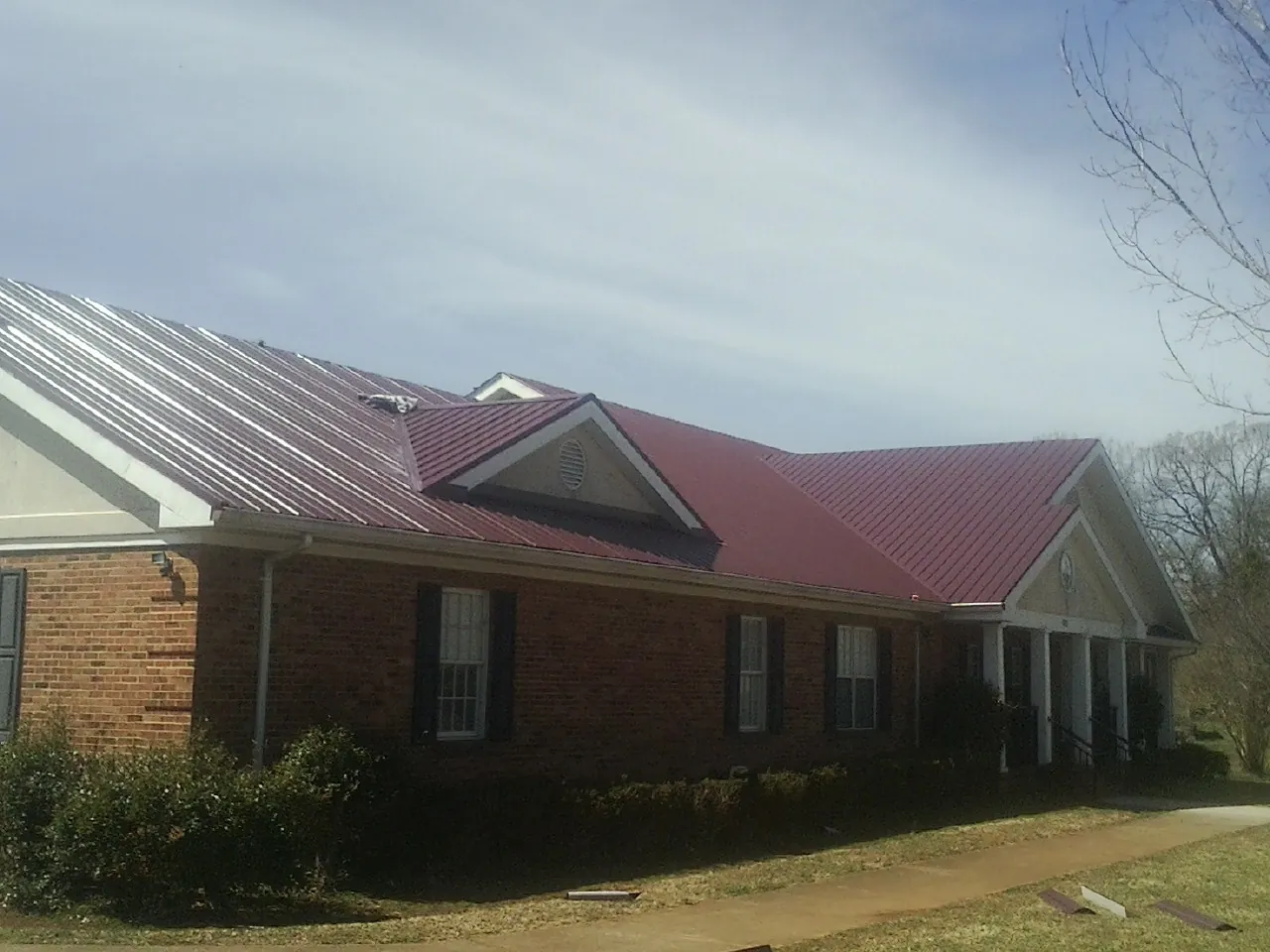 Red metal roof with gabled entries on a long brick building, from a Hail Damage Roof Repair job in Strawberry Plains
