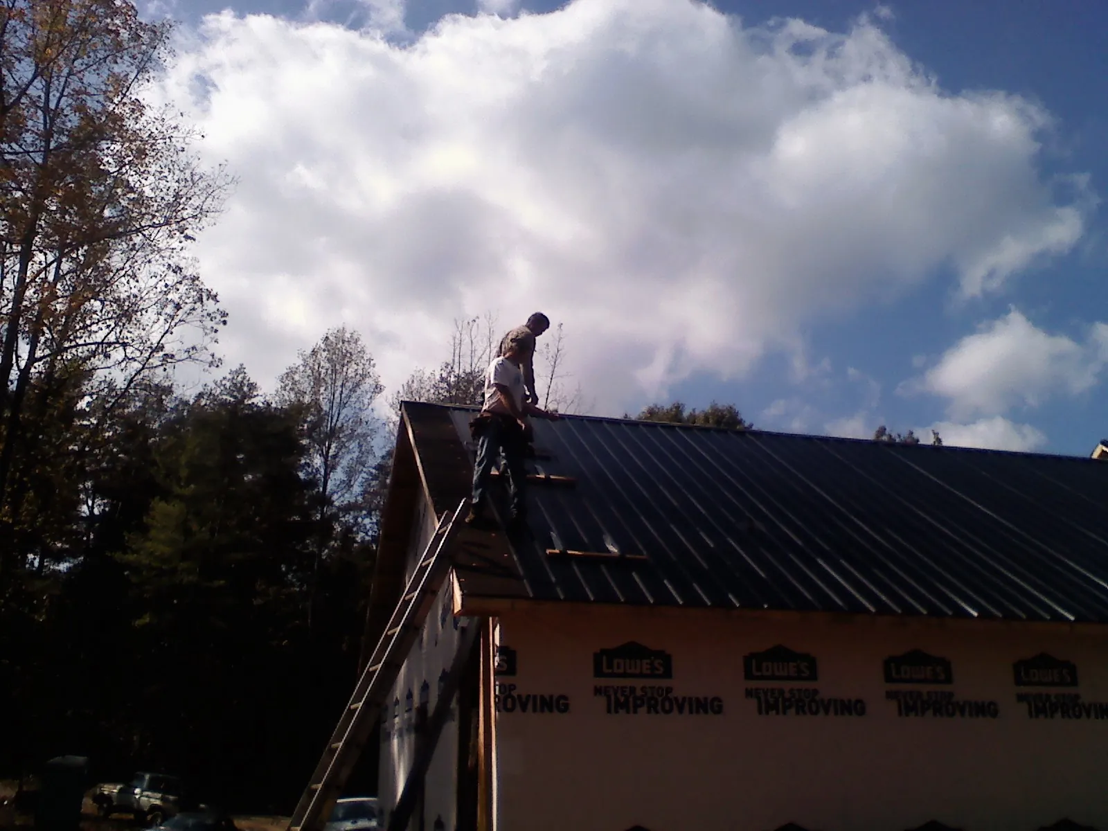 Roofer fastening dark metal panels high against a cloudy sky, from a Roof Inspection job in Strawberry Plains