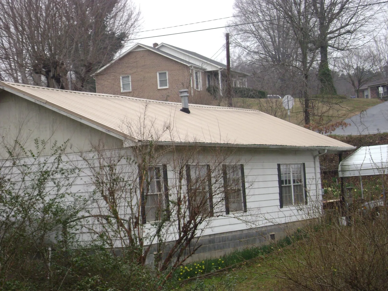 Tan metal roof on a white sided house set into a hillside — Commercial Roofing by Roofing Brothers in Strawberry Plains