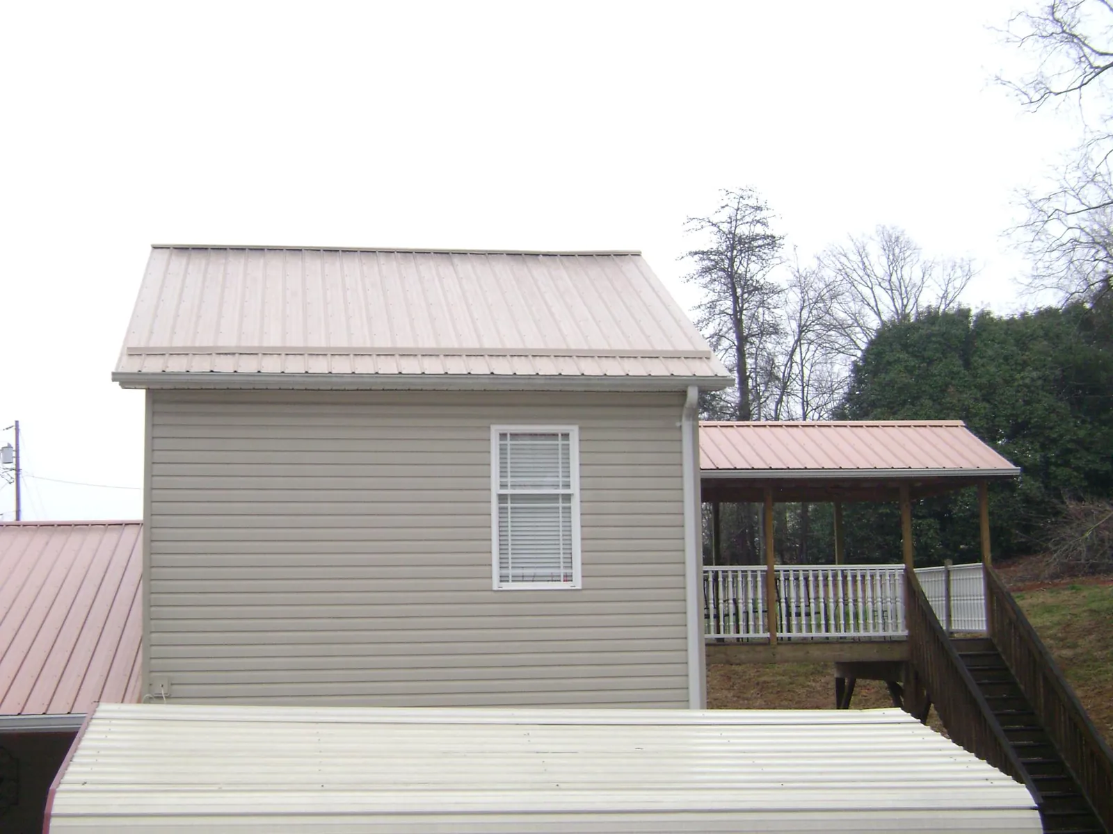 Tan metal roofs on a two story addition and attached porch, from a Roof Replacement job in Strawberry Plains